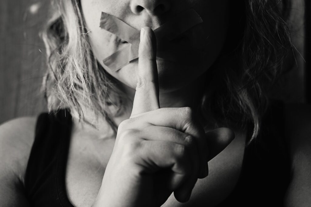 foto em preto e branco de mulher com o indicador na frente dos lábios cerrados, fazendo sinal de silêncio